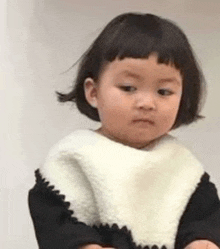 a little girl with short hair is wearing a bib and a black and white sweater .