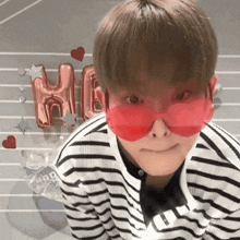 a young man wearing red sunglasses with the letter h on a balloon in the background