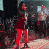 a woman is singing into a microphone while a man plays a guitar behind her .