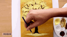 a person is painting a tree on a piece of paper with drawbook written on it