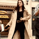 a woman in a trench coat is walking in front of a store that says talabella