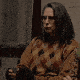 a woman wearing glasses and a plaid sweater holds a card