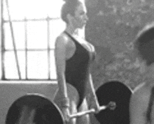 a black and white photo of a woman lifting a barbell in a gym .