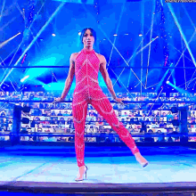 a woman in a red jumpsuit stands on one leg in front of a crowd
