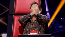 a man is covering his face with his hands while sitting in a chair