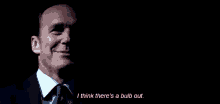a man in a suit and tie is talking in the dark and saying `` i think there 's a bulb out '' .