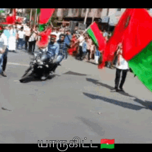 a man riding a motorcycle with a green and red flag in front of a crowd of people