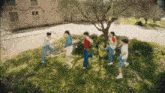 a group of young people are dancing in the grass in front of a house .