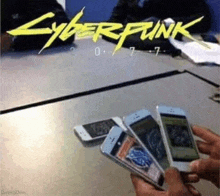 a person is holding four cell phones in front of a cyberpunk 2077 poster