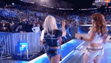 two women are dancing on a stage in front of a crowd at a wrestling match .