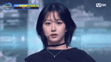 a girl with a choker looks at the camera with a mnet logo behind her