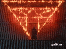 a man in a black cape stands in front of a wall that is on fire and says keluarga man on the bottom right