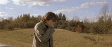 a man in a jacket is standing in a field with his hands on his face .