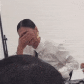 a woman in a white shirt and tie is covering her face .