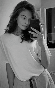 a black and white photo of a woman taking a selfie in front of a mirror .