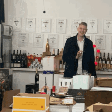 a man stands in front of a wall with awards on it and boxes of champagne