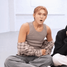 a man in a grey tank top sits on the floor