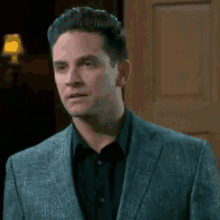 a man in a suit and black shirt stands in front of a door