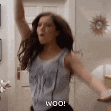 a woman is dancing in a room with her arms outstretched and the word woo written on the screen .