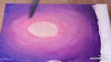 a person is painting a purple and pink circle on a piece of paper
