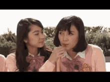 two girls in school uniforms are talking to each other and one is eating something .