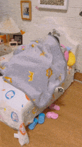 two cats are laying under a blanket on a bed . one of the cats is licking the other 's face .