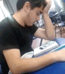 a man in a black shirt is sitting at a desk with his head in his hands