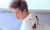a close up of a young man with curly hair wearing a white shirt and earring .