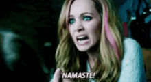 a woman with pink hair is screaming and saying namaste in a dark room .