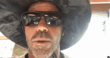 a man with a beard wearing sunglasses and a large hat