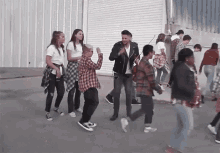 a group of people are walking down a street with a man in a leather jacket playing a violin