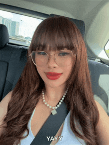a woman wearing glasses and a pearl necklace is sitting in the back seat of a car