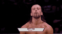 a wrestler named rhett titus is standing in a ring with his hand in the air .