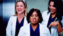 three female doctors are standing next to each other laughing and pointing at something .