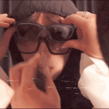 a person wearing sunglasses and a ring on their finger is covering their face