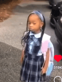 a little girl in a school uniform is standing on a sidewalk next to a car .