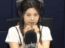 a woman wearing headphones sits in front of a microphone and looks at the camera