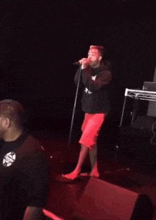 a man in red shorts singing into a microphone on stage