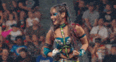 a female wrestler is standing in front of a crowd with her arms outstretched and smiling .