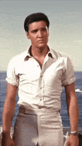 a man in a white shirt and khaki pants is standing in front of the ocean