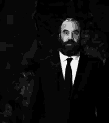 a black and white photo of a man with a beard wearing a suit and tie making a funny face .