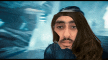 a man with long hair and a beard looks at the camera with a blurry background