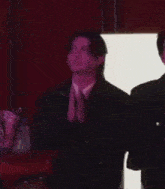 a man in a suit is clapping his hands while standing next to another man .