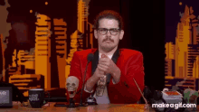 a man in a red suit is sitting at a desk with a make a gif.com logo on the bottom