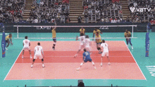 a group of volleyball players are playing a game on a court with a crowd watching .