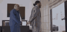 a man in a suit is standing next to another man in a blue shirt in a living room .