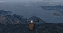 a man sits on a ledge overlooking mountains and a body of water