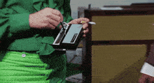 a woman in green pants is holding a small device with the word nintendo on it
