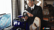 a man is reading a book while sitting in a chair with a nbc logo on it
