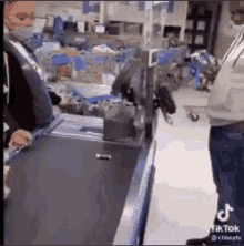 a man wearing a mask is standing next to a cash register in a store .